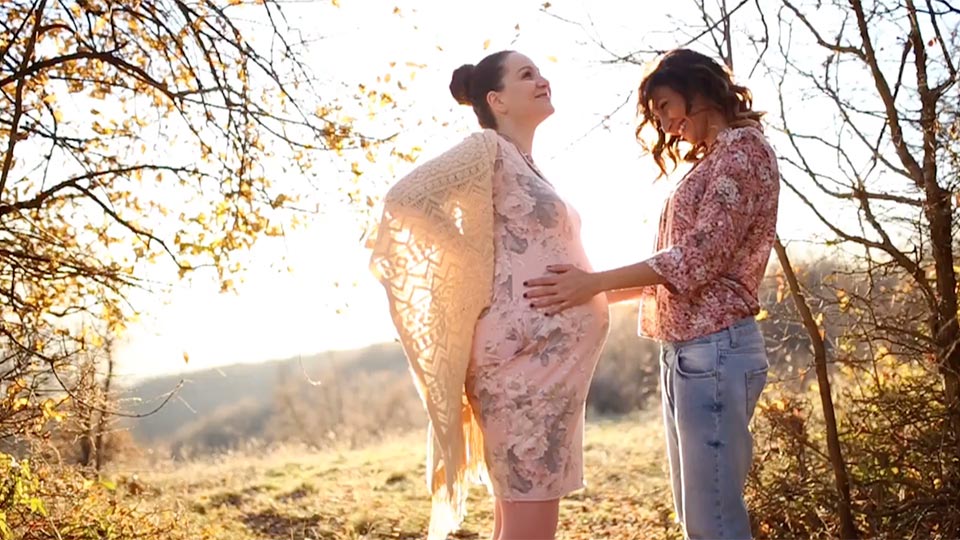 Two lesbians embracing. One is pregnant.