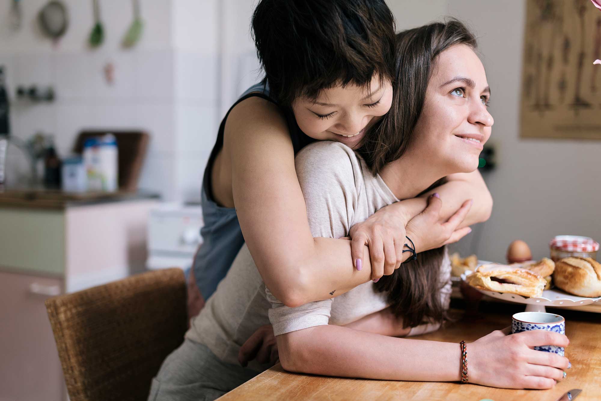 Hopeful, happy, lesbian couple embracing over coffee